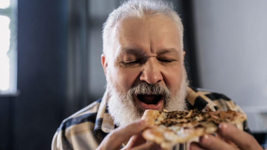 older man open his mouth to eat a slice of pizza